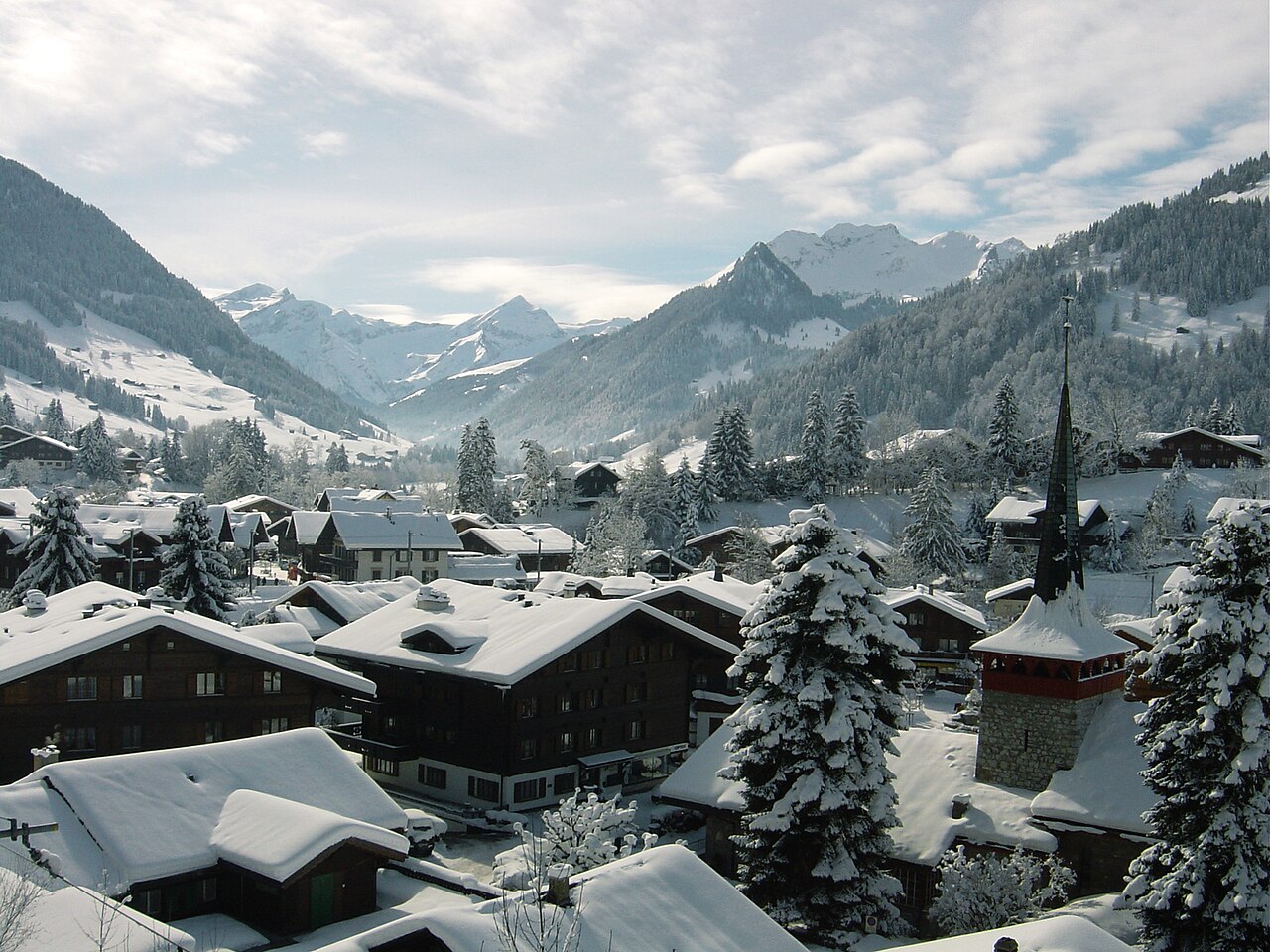 Snow-covered alpine village of Gstaad with chalets and a church spire.