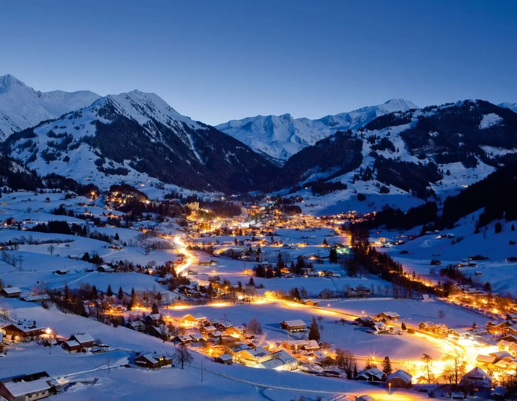Gstaad village glowing at twilight, nestled in the snow-covered alpine valley.